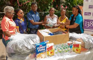 House Mother at the Annie Dawson Children's Home, Eletha Gardner, (centre) and Sonia Gibbs, caregiver, (2nd right) accepts items from Leslie Robinson Hall, Resident Advisor Jahmel Brown, 3rd left during a visit to the Home on December 20. Looking on from left are 138SL Resident Relations Chief, Marva Thompson, Montacher Pierre, Deputy Hall Chair, Leslie Robinson Hall and 138SL Public Relations and Marketing Manager, Karelle McCormack, (far right).